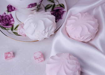 A delicious marshmallow lies near the cup and on a saucer. A colorful, sweet treat for tea