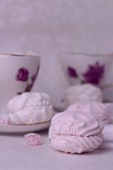 Picture in pink tone. marshmallows and sweets, which lie on a silk fabric against the background of beautiful cups with a floral ornament. Blur effect.