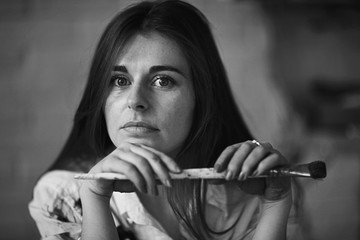 Portrait of a young adult female artist black background with a brush