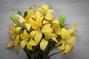  Bouquet of bright yellow lilies on a light wooden background.