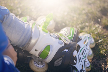  A child shod in rollers sits on the grass. Close-up shoes.
