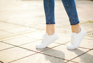 Woman in white sneakers on asphalt at sunset.