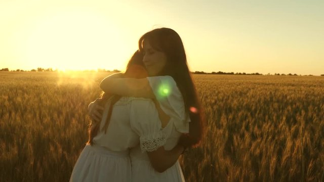 Mom gently hugs daughter against backdrop of a beautiful sunset. happy family concept. adult daughter in arms of her mother in field in the rays of the sun. mom strokes her daughter's hair