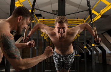 Naklejki  Muskularni mężczyźni podciągają się na kółkach gimnastycznych