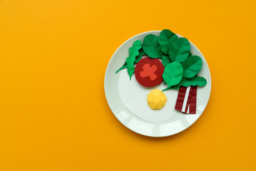 Continental breakfast made from paper: fried egg, tomato, bacon, spinach and arugula on yellow background. Minimal, creative, healthy or food art concept. Copy space. Top view