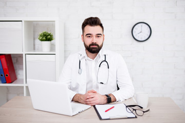 portrait of male doctor using laptop in office