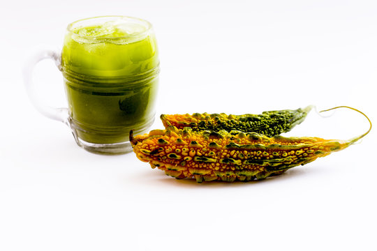 Raw organic bitter melon or bitter gourd with its extracted juice in a transparent glass with some ice cubes in it isolated on white.