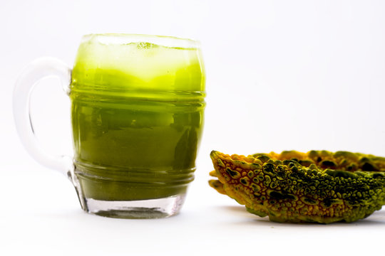 Raw organic bitter melon or bitter gourd with its extracted juice in a transparent glass with some ice cubes in it isolated on white.
