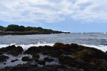 Waves Crashing on Rocky Shore in Hawaii white foam as the waves wash over the rocks under a blue sky