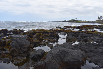 Fototapeta na wymiar Waves Crashing on Rocky Shore in Hawaii white foam as the waves wash over the rocks under a blue sky