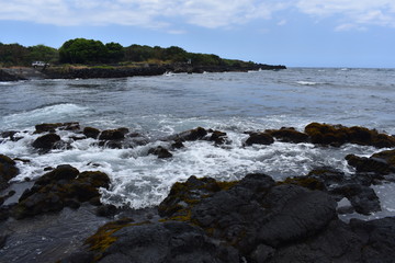 Waves Crashing on Rocky Shore in Hawaii white foam as the waves wash over the rocks under a blue sky