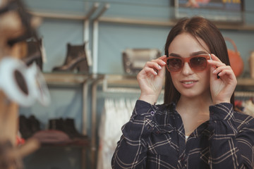 Attractive young woman trying on sunglasses at fashion shop, copy space. Beautiful female customer buying new eyewear at optician shop, copy space