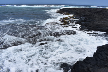 Waves Crashing on Rocky Shore in Hawaii white foam as the waves wash over the rocks under a blue sky