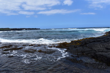 Waves Crashing on Rocky Shore in Hawaii white foam as the waves wash over the rocks under a blue sky