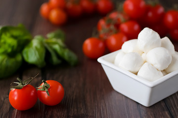 Mozzarella cheese, basil and cherry tomatoes on  brown wooden table. Ingredients for making salad caprese. Mediterranean Kitchen.