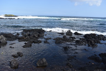Waves Crashing on Rocky Shore in Hawaii white foam as the waves wash over the rocks under a blue sky