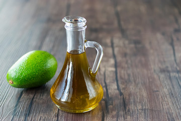 Avocado oil in glass jug on  brown wooden background. Healthy food.