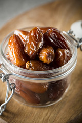 Dried dates in a glass jar on a light grey marble table.