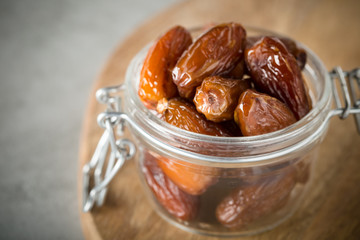 Dried dates in a glass jar on a light grey marble table.