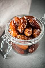 Dried dates in a glass jar on a light grey marble table.