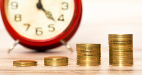 Spending money concept, gold coins stack with an alarm clock in the background