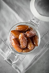 Dried dates in a glass jar on a light grey marble table.