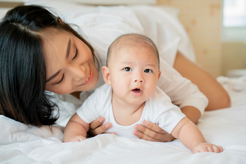Portrait Mother is taking care of newborn baby wearing clean white clothes In the bedroom. With love in mind to keep children healthy. And cheerful The child has good development. Mother's Day in May