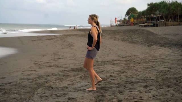 Young, fit woman stretching legs, doing warmup on the beach