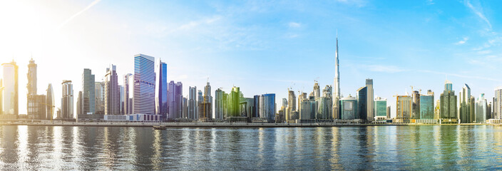 Stunning panoramic view of the Dubai skyline with the magnificent Burj Khalifa and many other buildings, skyscrapers and towers reflected on the Dubai water canal flowing in the foreground. Dubai