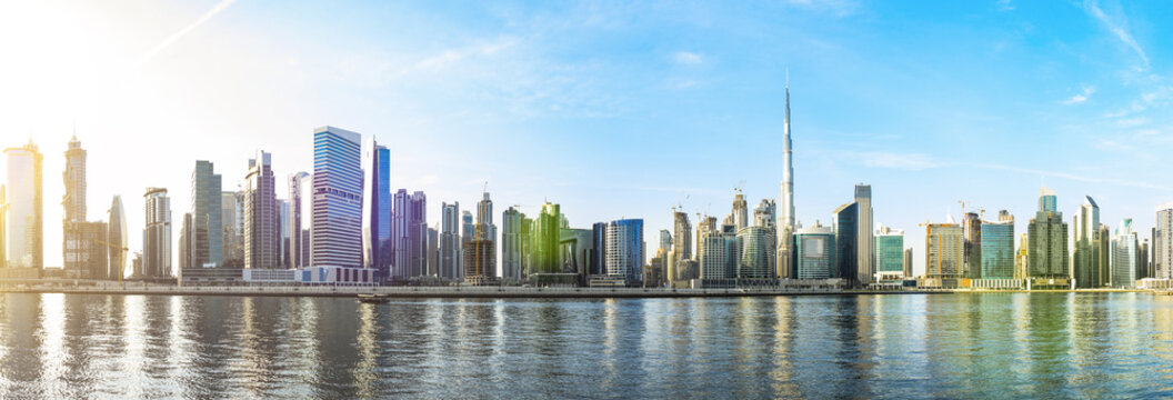 Stunning panoramic view of the Dubai skyline with the magnificent Burj Khalifa and many other buildings, skyscrapers and towers reflected on the Dubai water canal flowing in the foreground. Dubai