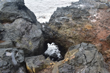 Waves Crashing on Rocky Shore in Hawaii white foam as the waves wash over the rocks under a blue sky