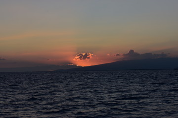 Bright sky at sunset over the Pacific Ocean in Hawaii Sun dipping behind mountain and cloud throwing all sorts of colors into the sky