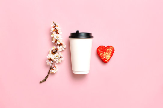 Coffee or tea paper cup, heart-shaped macaroon cakes, spring branches of white flowers on pink background top view flat lay. Take away coffee cup, mockup. Coffee love concept, layout for design