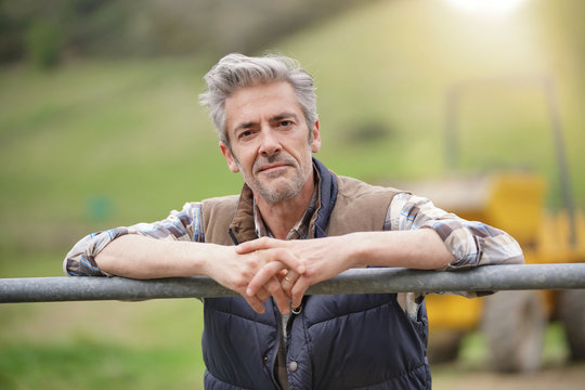Attractive farmer leaning on fence looking at camera