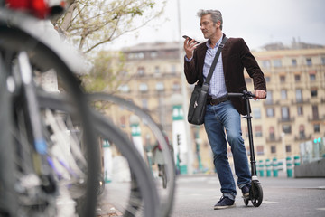 Businessman talking on cellphone commuting on micro scooter