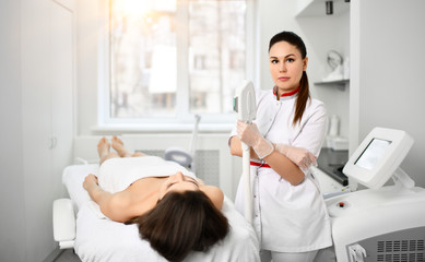 Fototapeta premium Doctor-cosmetician in white gown with a medical device is ready to perform a cosmetic procedur for a patient in beauty saloon
