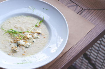 A plate of risotto with sprouts stands on a brown cafe table.