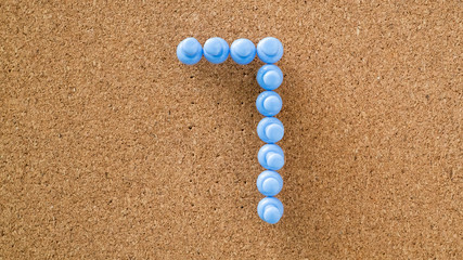 seven, number made by pastel blue pushpin on cork board texture, top view