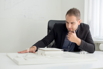 Businessman in the office is looking closely into the architecture of a modern house model