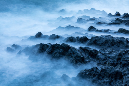 Waves crashing on the rocky shore and creating dreamy mist on the beach in Seychelles