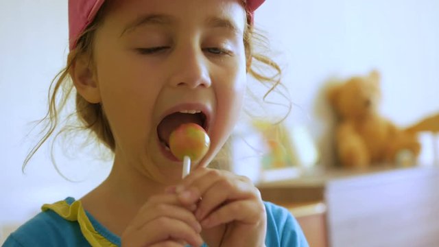Little girl enjoying a lollipop while staring at camera. Child eating candy, sweets, sugar