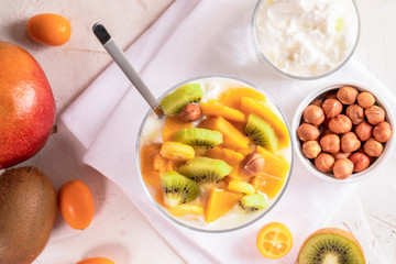 Glass bowl with yogurt, and fruits, glass of yogurt, bowl of nuts  on white napkin.