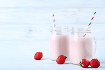 Strawberry smoothie in glass jars with straws on wooden table