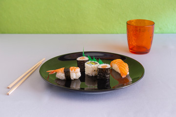 mixed sushi on black plate with orange glass and Japanese chopsticks
