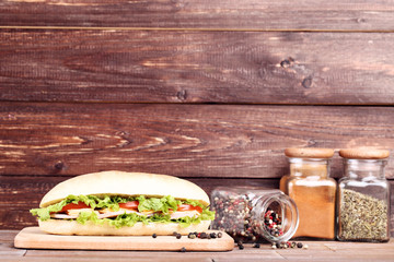 Fresh sandwich with seasonings in jars on brown wooden table
