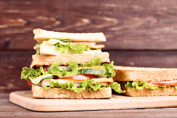 Tasty sandwiches with cutting board on brown wooden background