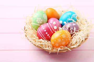 Colorful easter eggs in basket on pink wooden table