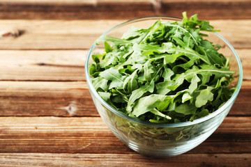 Green arugula leafs in glass bowl on brown wooden table