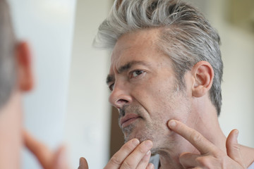 Fototapeta premium Portrait of mature handsome man looking in mirror at home