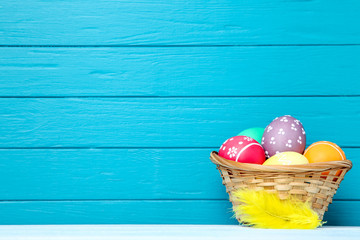 Colorful easter eggs in basket with yellow feather on blue background